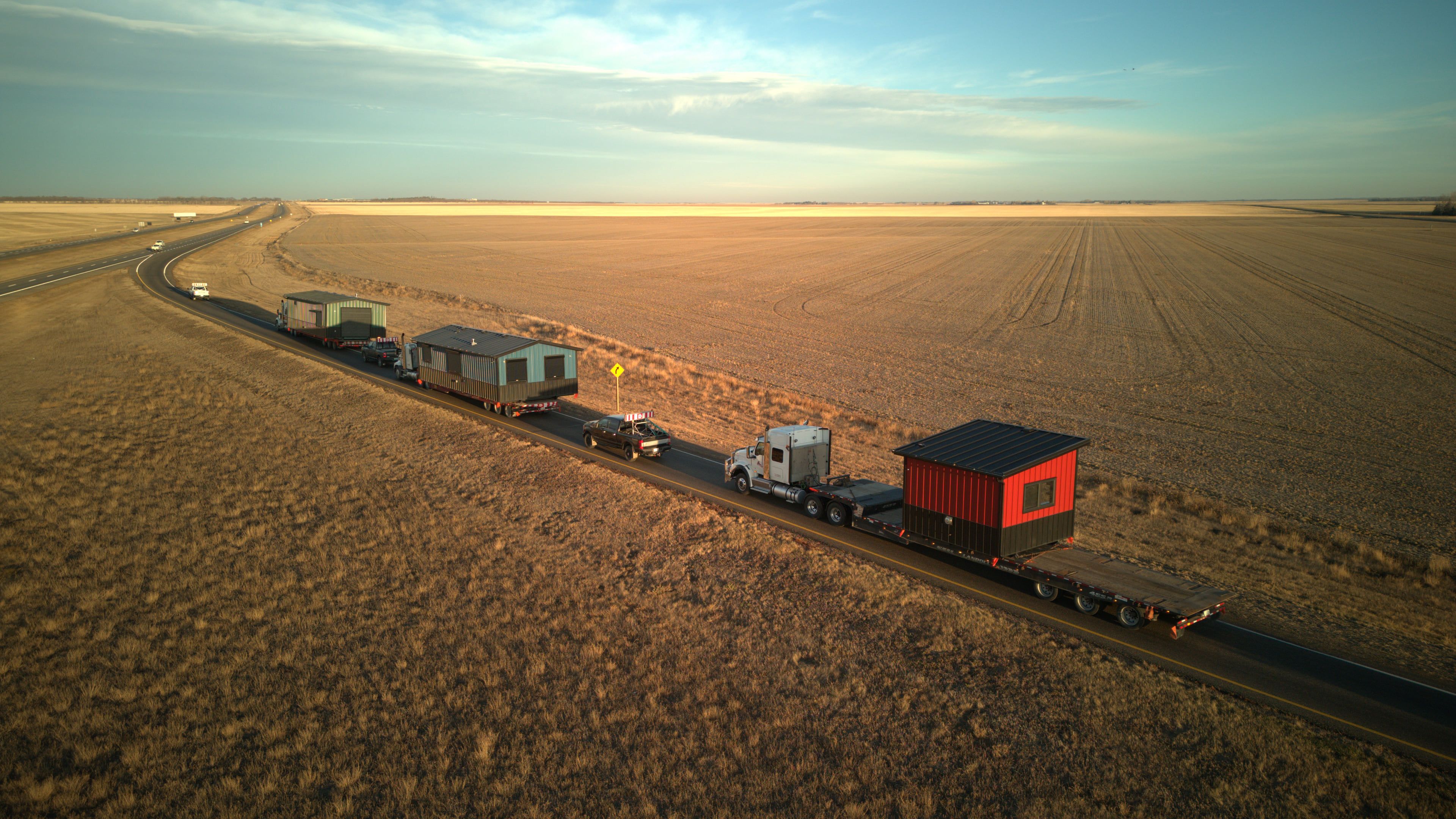 A convoy of Herauf modular units hauled along a prairie highway at golden hour, delivered across Canada