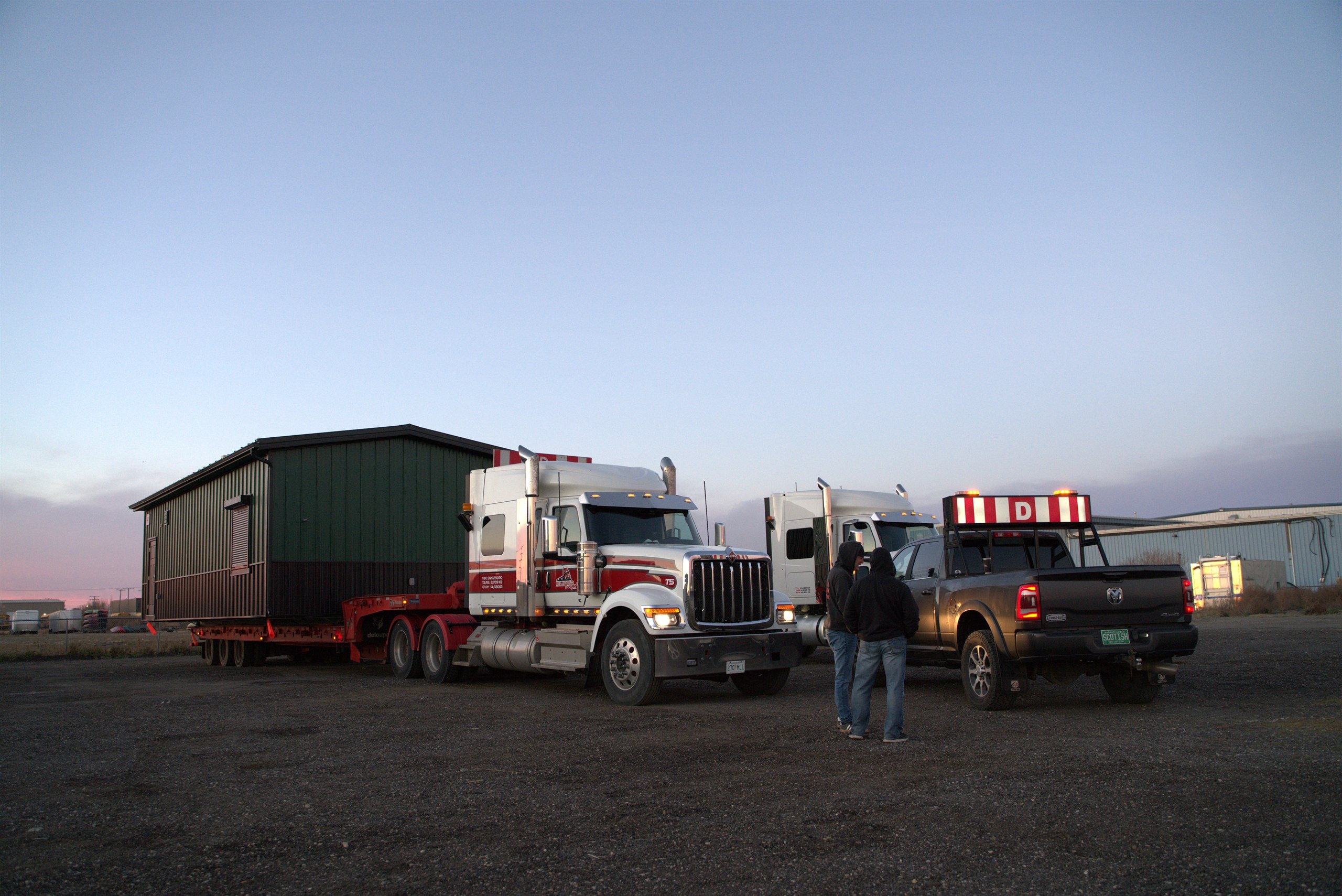 A Herauf modular unit loaded on a lowboy trailer at dusk, staged for delivery across Canada