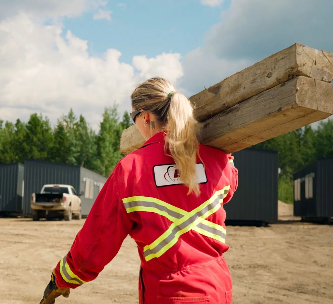 A Herauf site crew member carrying timber beams across a prepared camp site