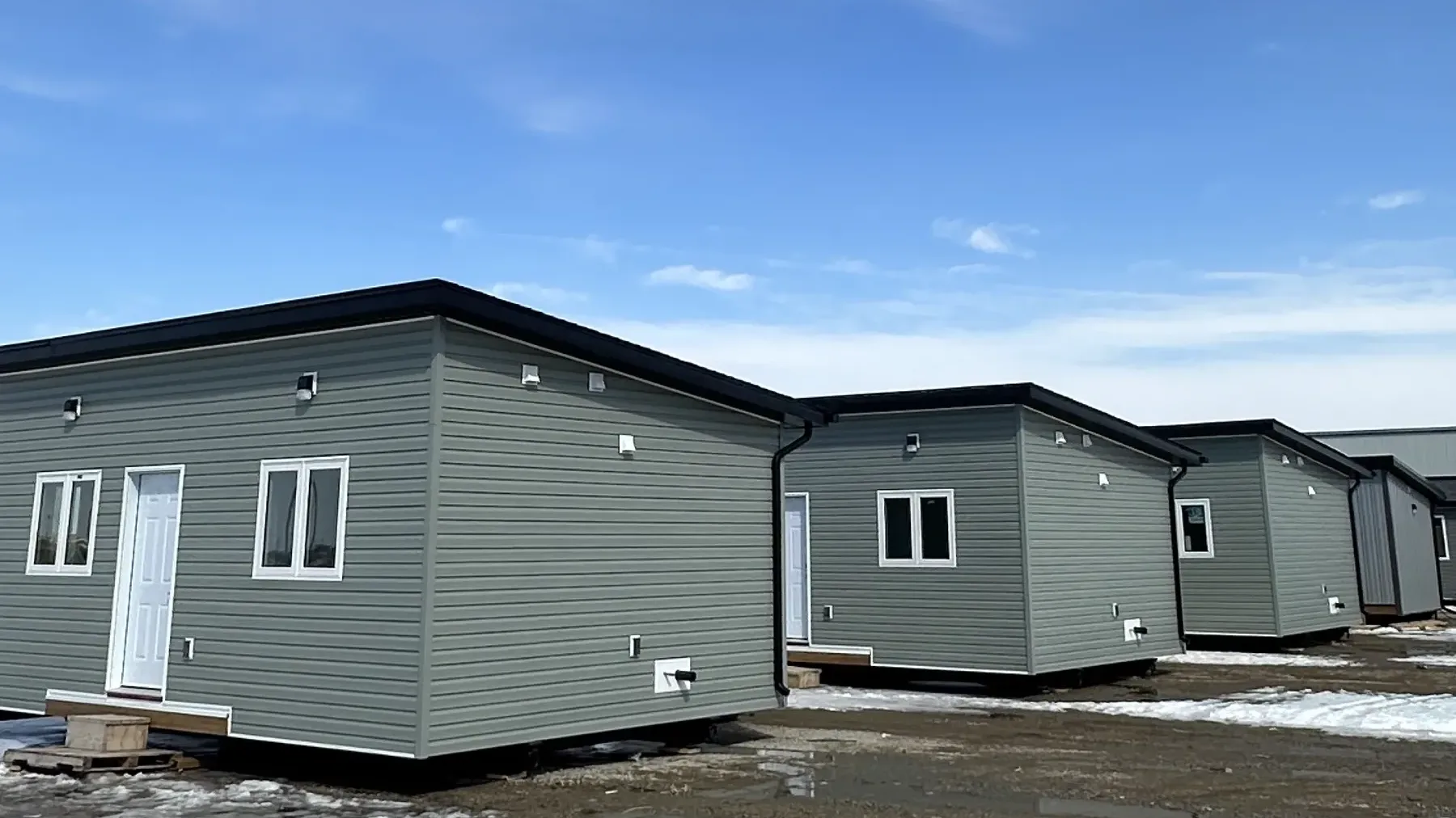 Three sage green modular units standing on temporary blocking in a thawing yard