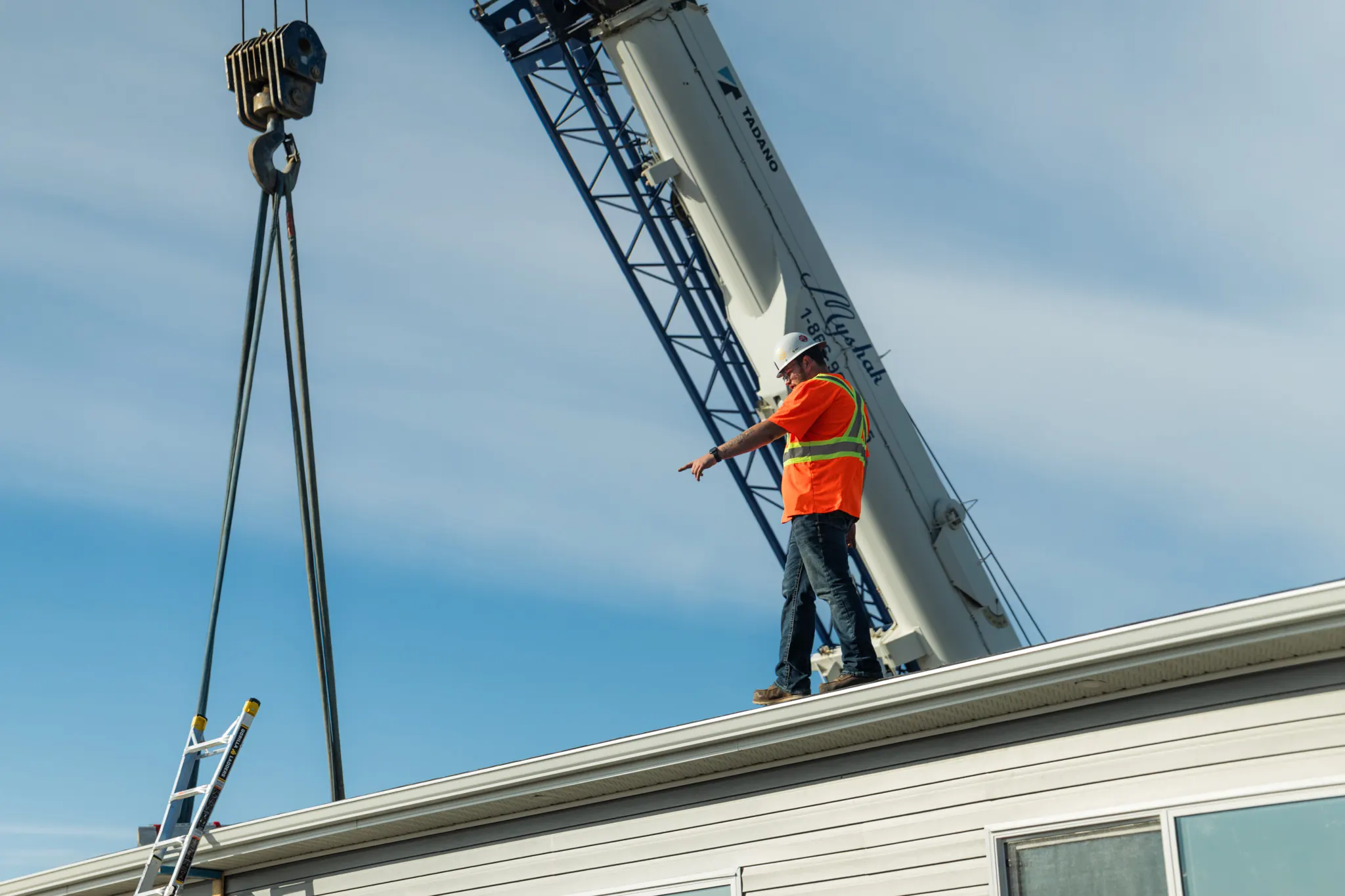 A crane hook and slings hanging over the module's roof while a crew member signals the operator