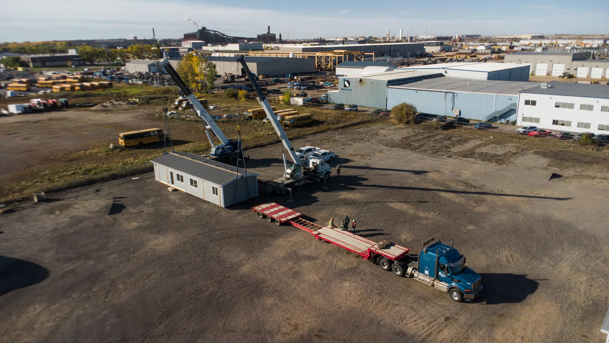 Drone view of the Zehner yard: a finished Herauf module on the ground beside two cranes and an empty lowboy trailer