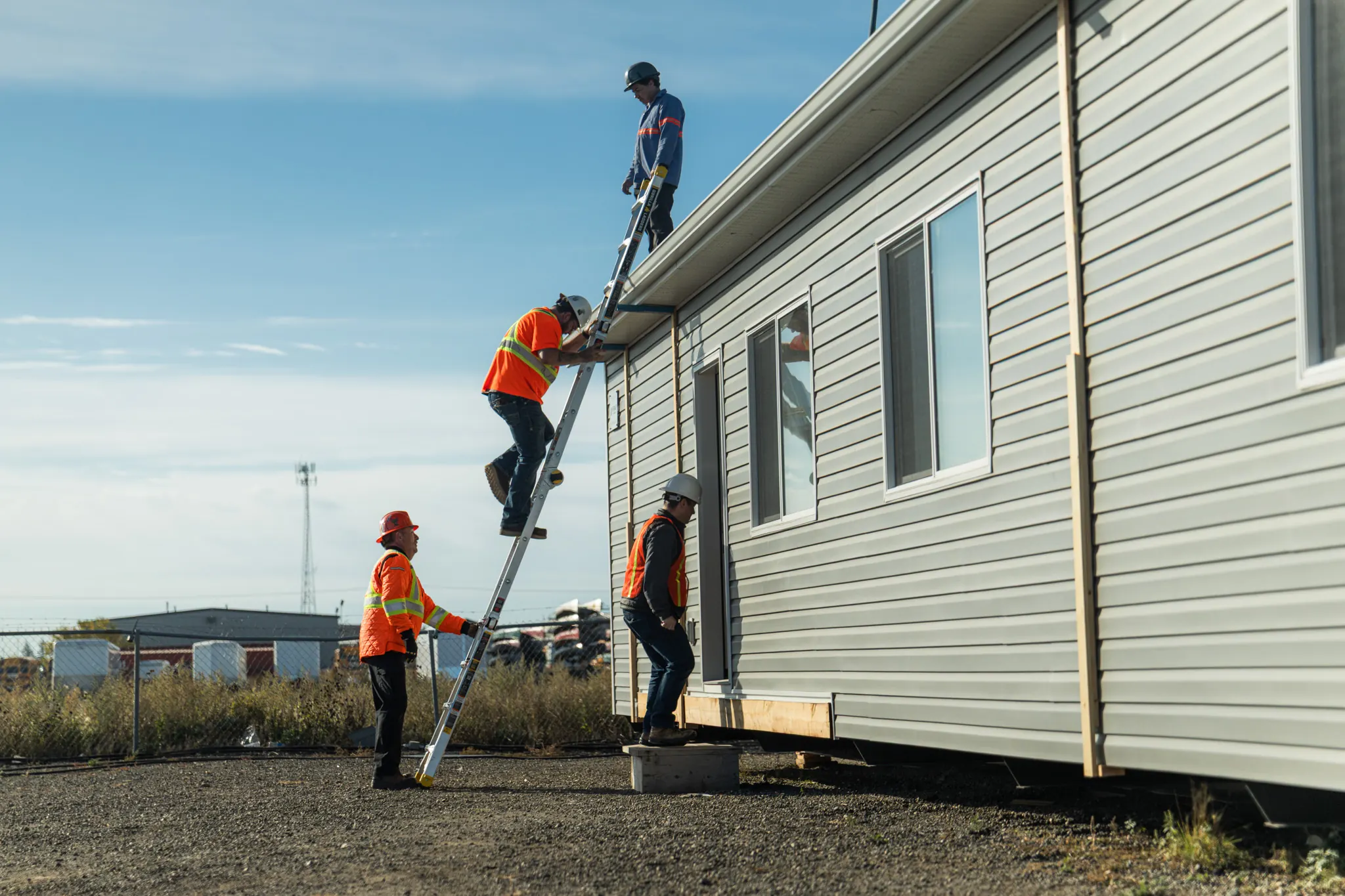 Crew in high-visibility gear climbing a ladder to the roof of the module to rig it