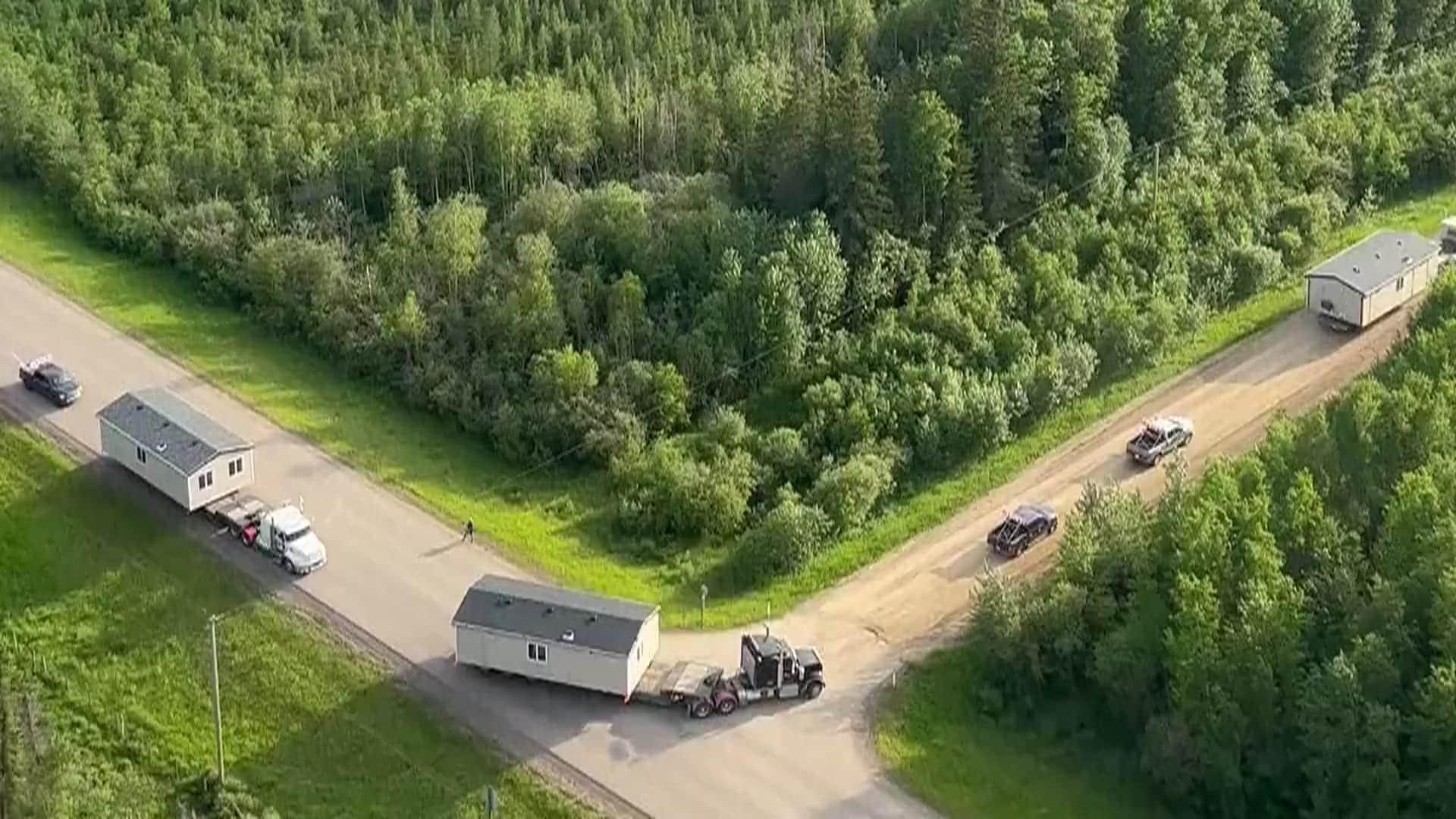 An aerial view of modular buildings hauled along a highway through northern boreal forest