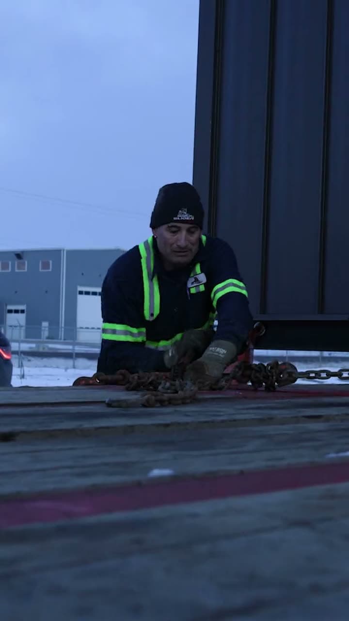 Crew member chaining down a load on a trailer at dusk