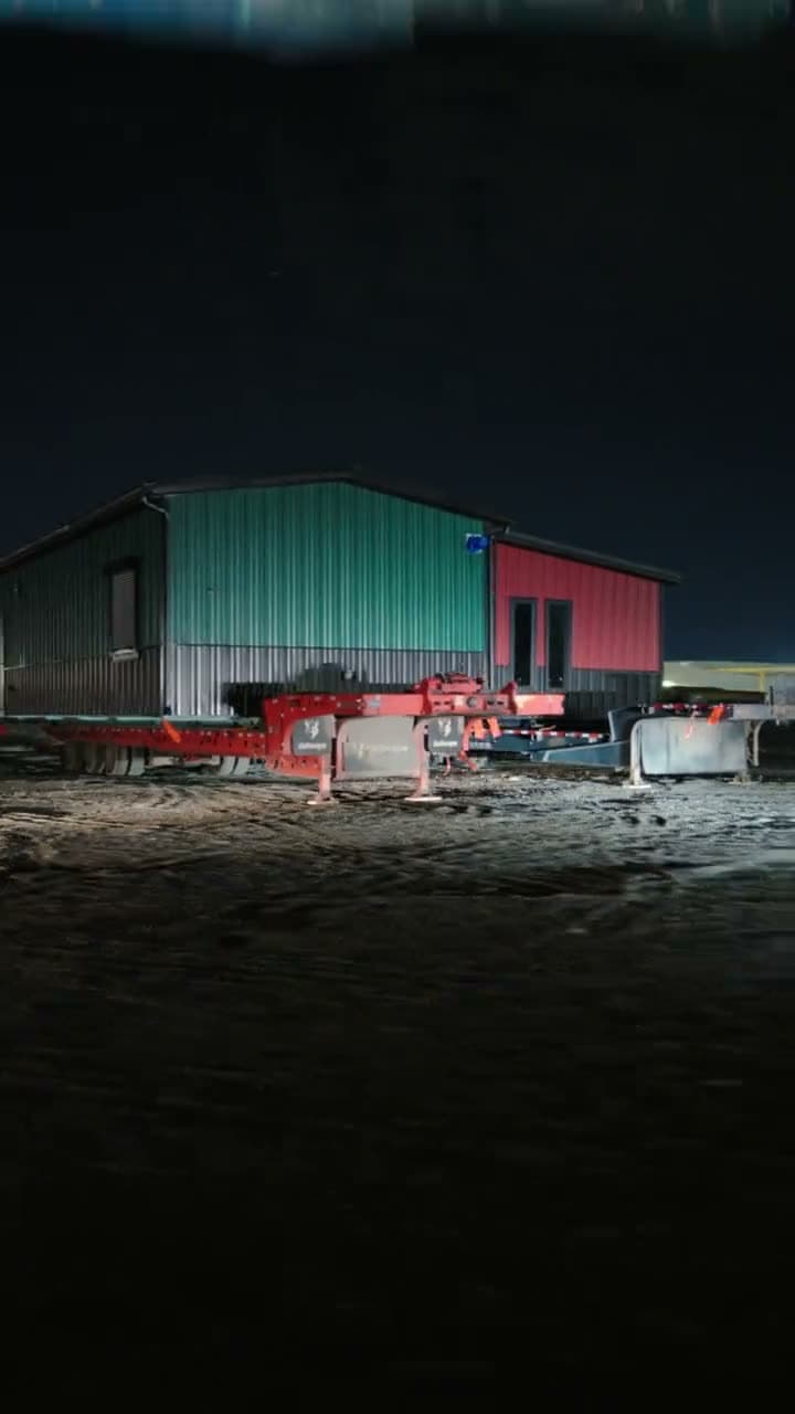 Teal and red metal-clad building on a trailer under yard lights at night