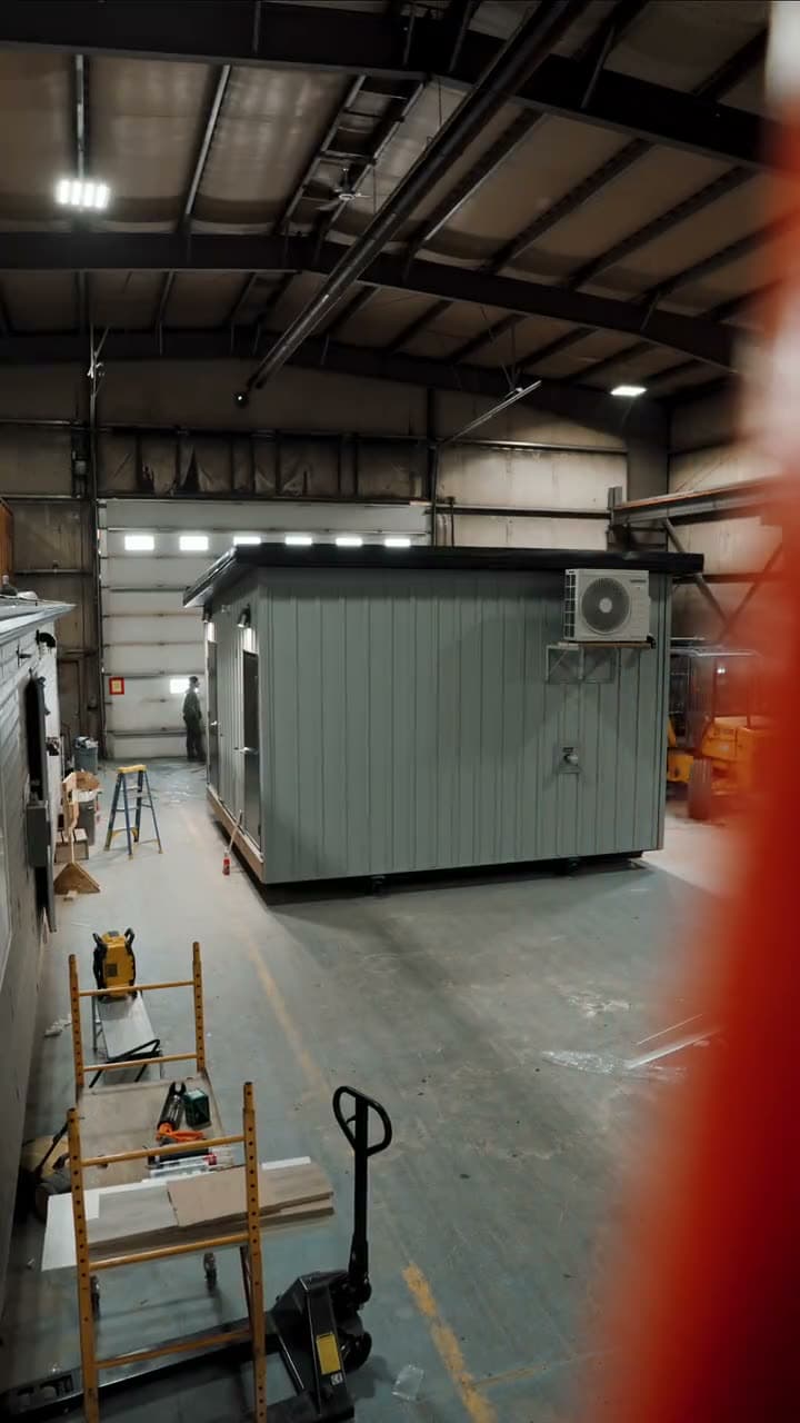 Grey washroom module on the plant floor with a ladder and pallet jack beside it