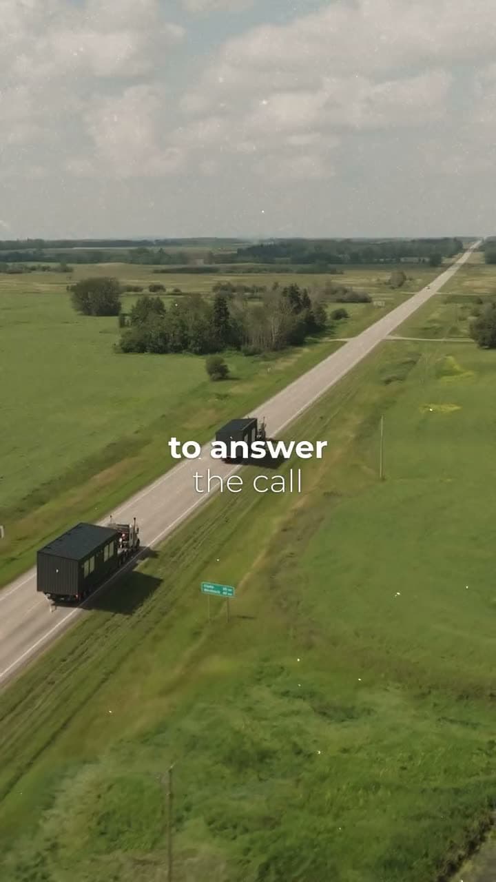 Drone view of a dark modular unit on a truck on a highway through green farmland