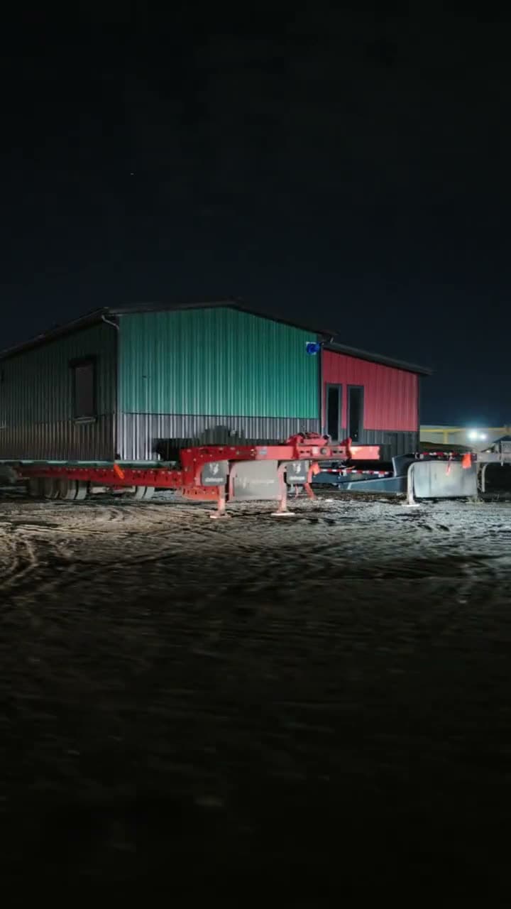Metal-clad building on a trailer, lit up in the yard at night