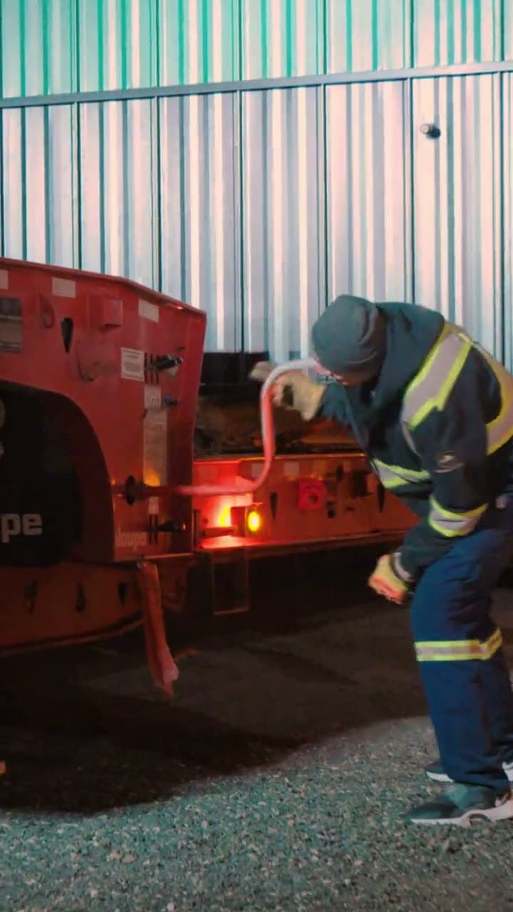 Crew member bent over a trailer's tail lights beside a metal building at night