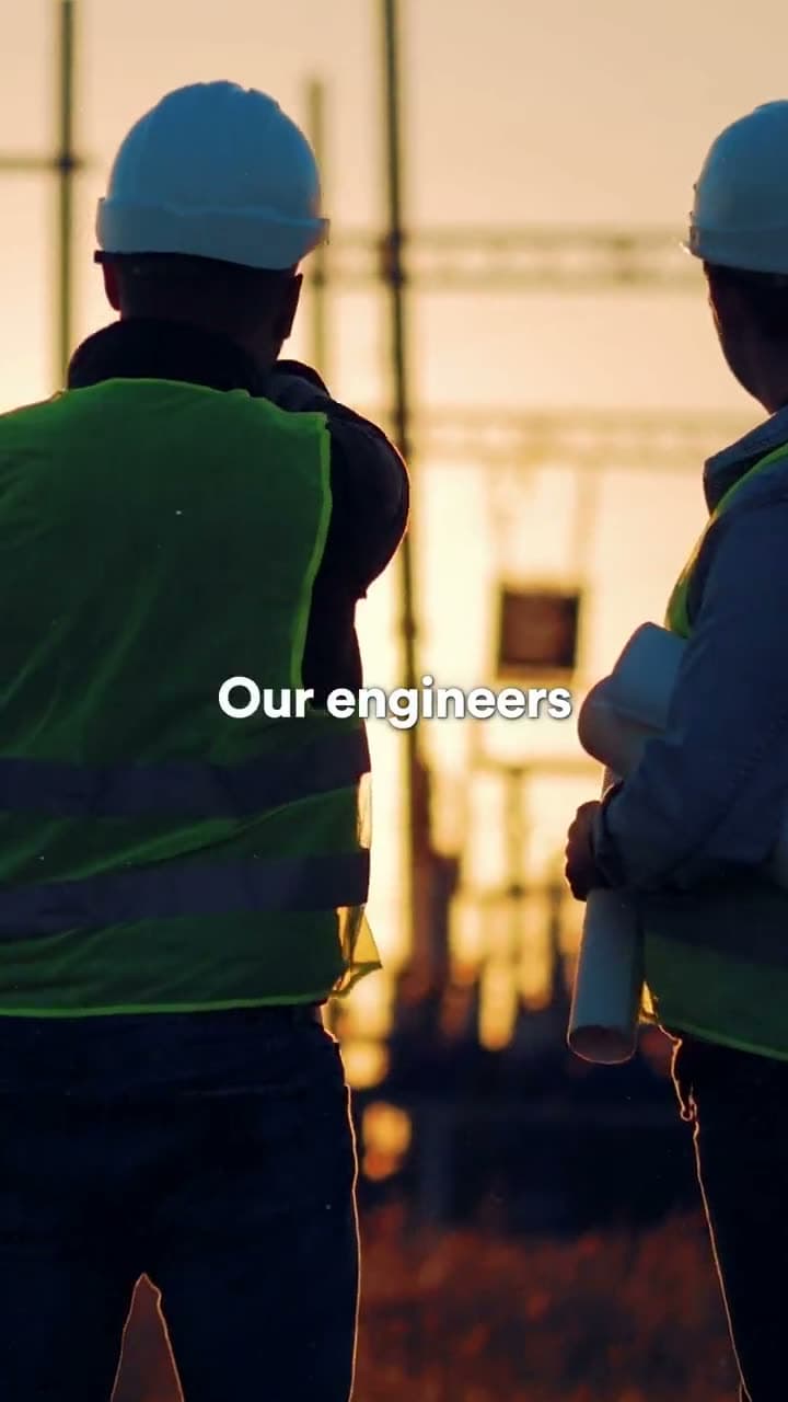 Two workers in hard hats and safety vests silhouetted against a sunset