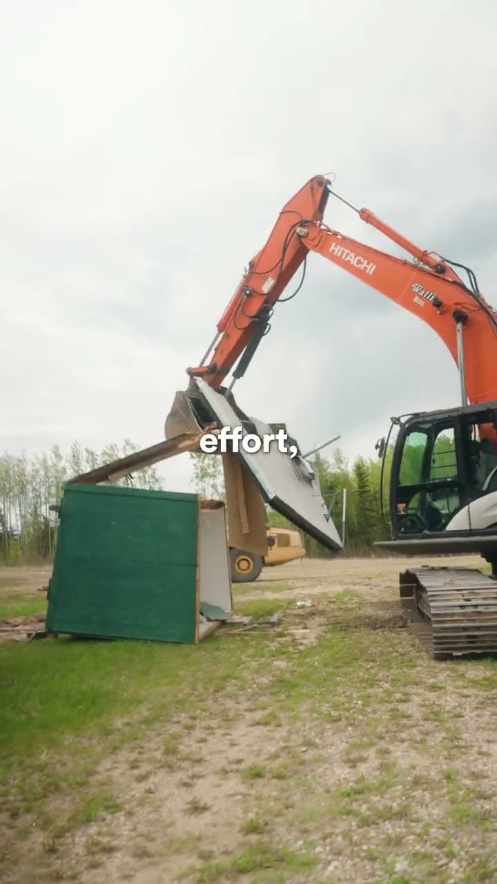 Excavator working beside a green modular unit on a grassy lot