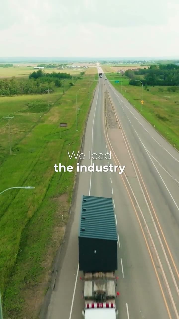 Drone view of a truck carrying a green module along a two-lane prairie highway