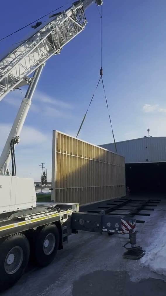 A crane lifting a framed wall section outside the plant