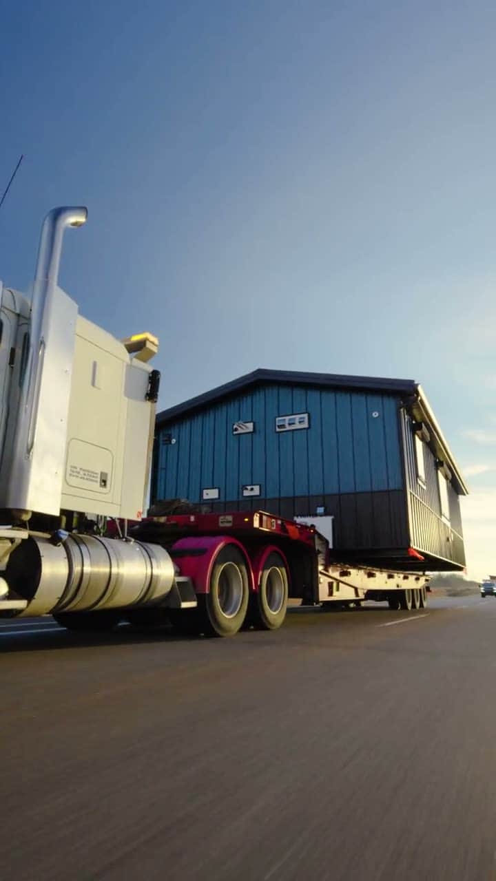 A finished building on a lowboy trailer crossing a prairie highway