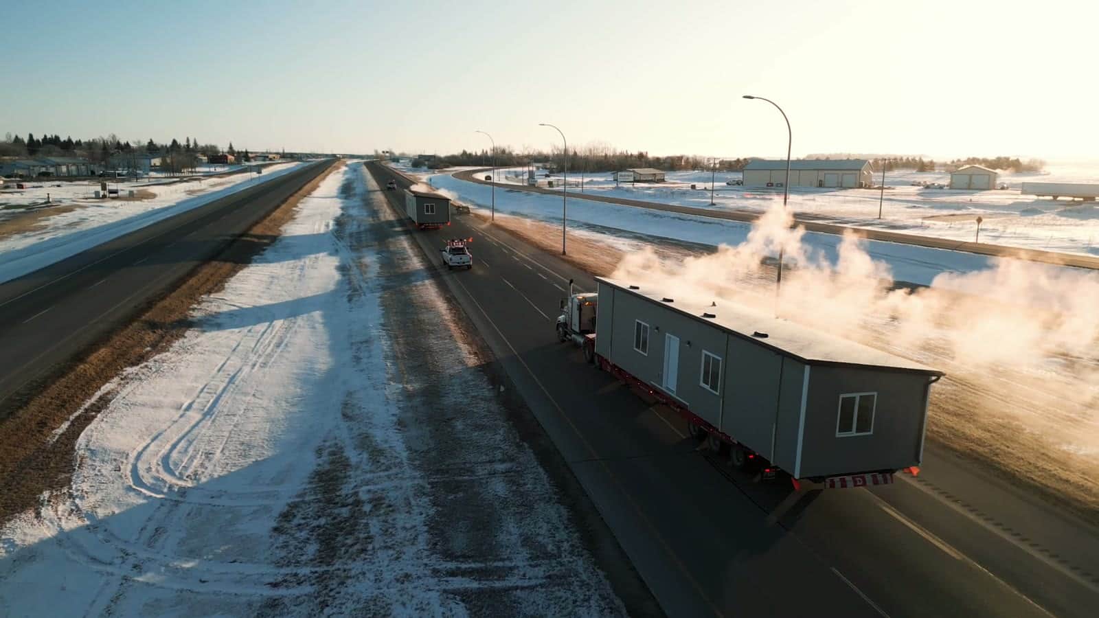 Finished homes travelling a snowy divided highway behind a pilot truck